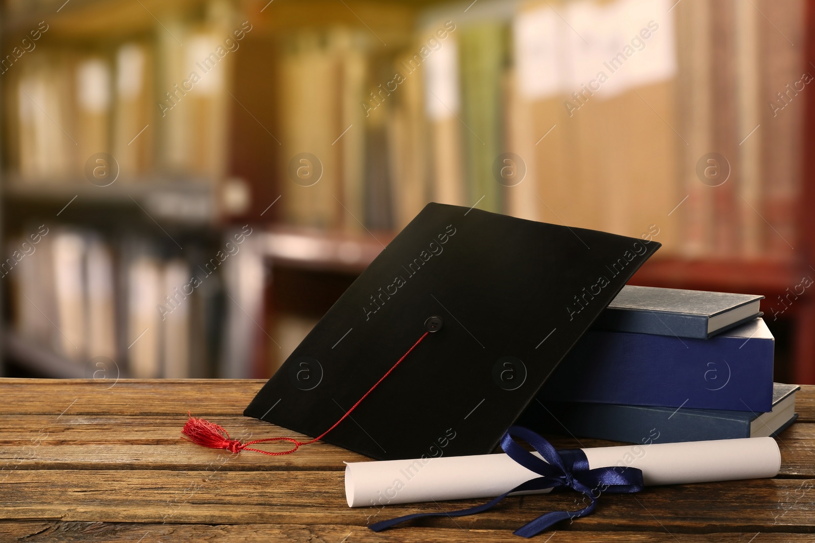 Image of Graduation hat, books and diploma on wooden table in library