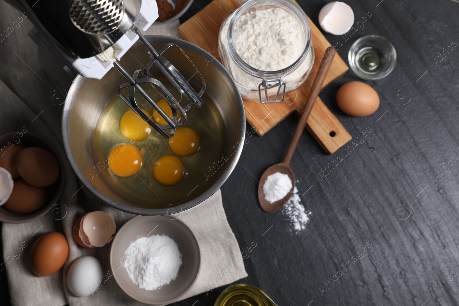 Photo of Making dough. Raw eggs in bowl of stand mixer and ingredients on black table, flat lay