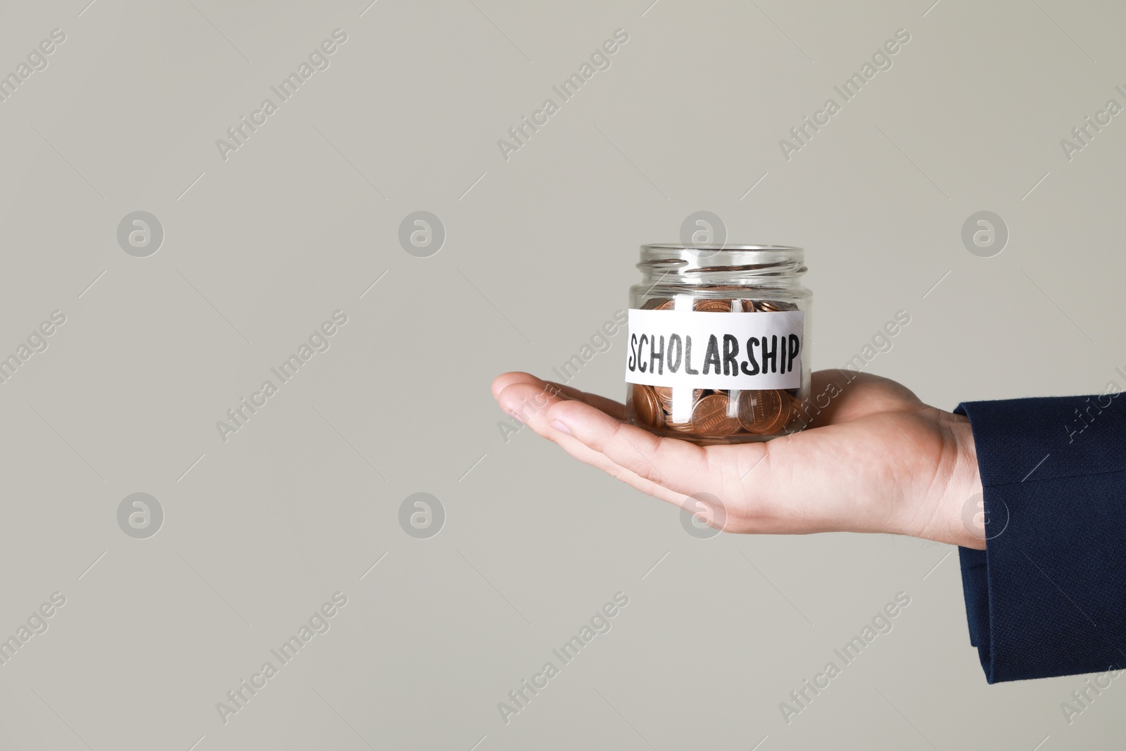 Photo of Man holding glass jar with coins against grey background, closeup and space for text. Scholarship concept