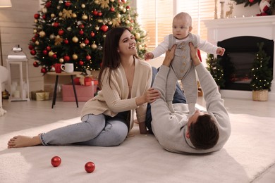 Happy family with cute baby on floor in room decorated for Christmas