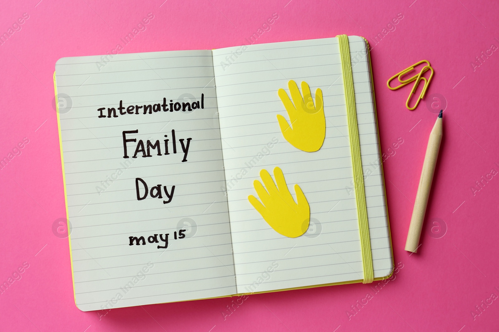 Photo of Notebook with text International Family Day May 15, pencil and paper clips on pink background, flat lay