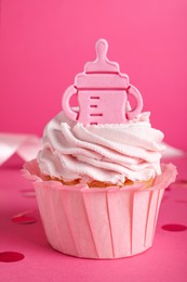 Photo of Beautifully decorated baby shower cupcake for girl with cream and topper on pink background, closeup
