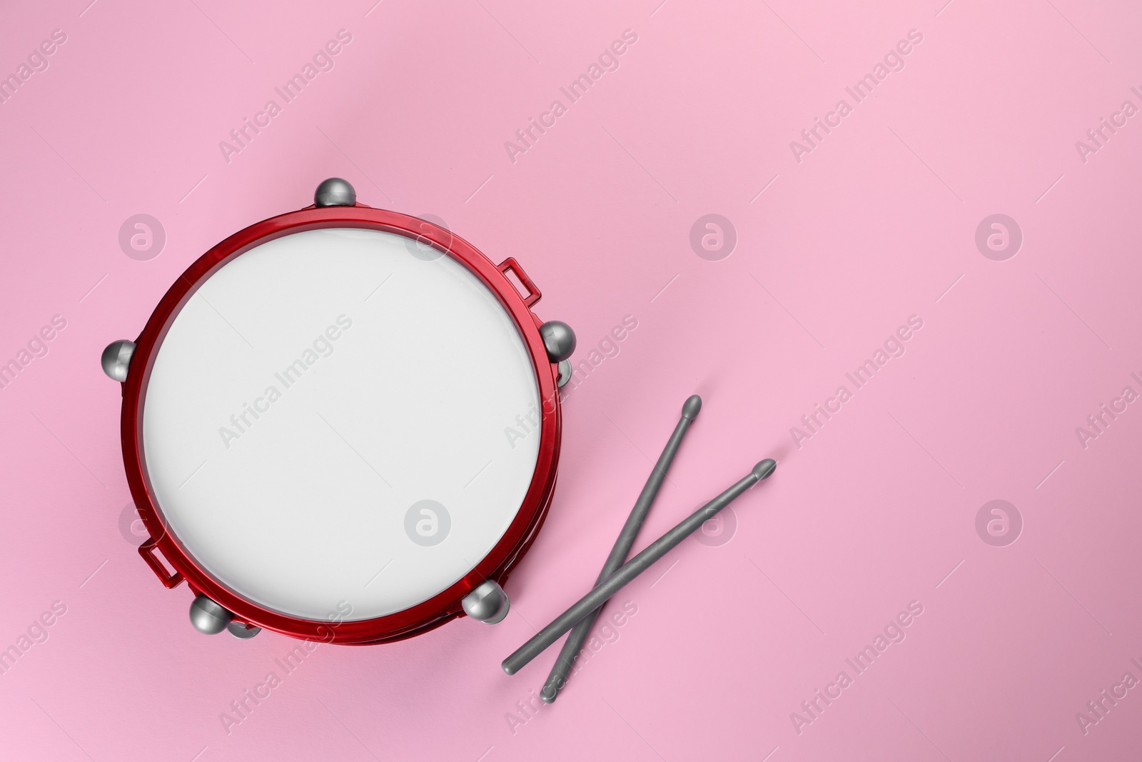 Photo of Children's drum with drumsticks on pink background, top view. Space for text