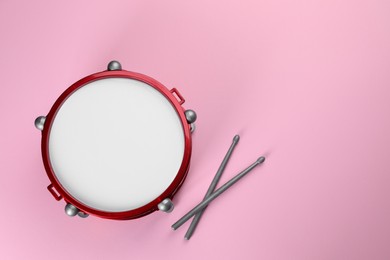 Children's drum with drumsticks on pink background, top view. Space for text