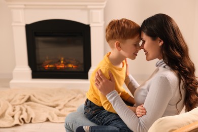 Happy mother and son spending time together near fireplace at home