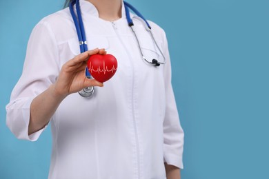 Doctor holding red heart on light blue background, closeup 