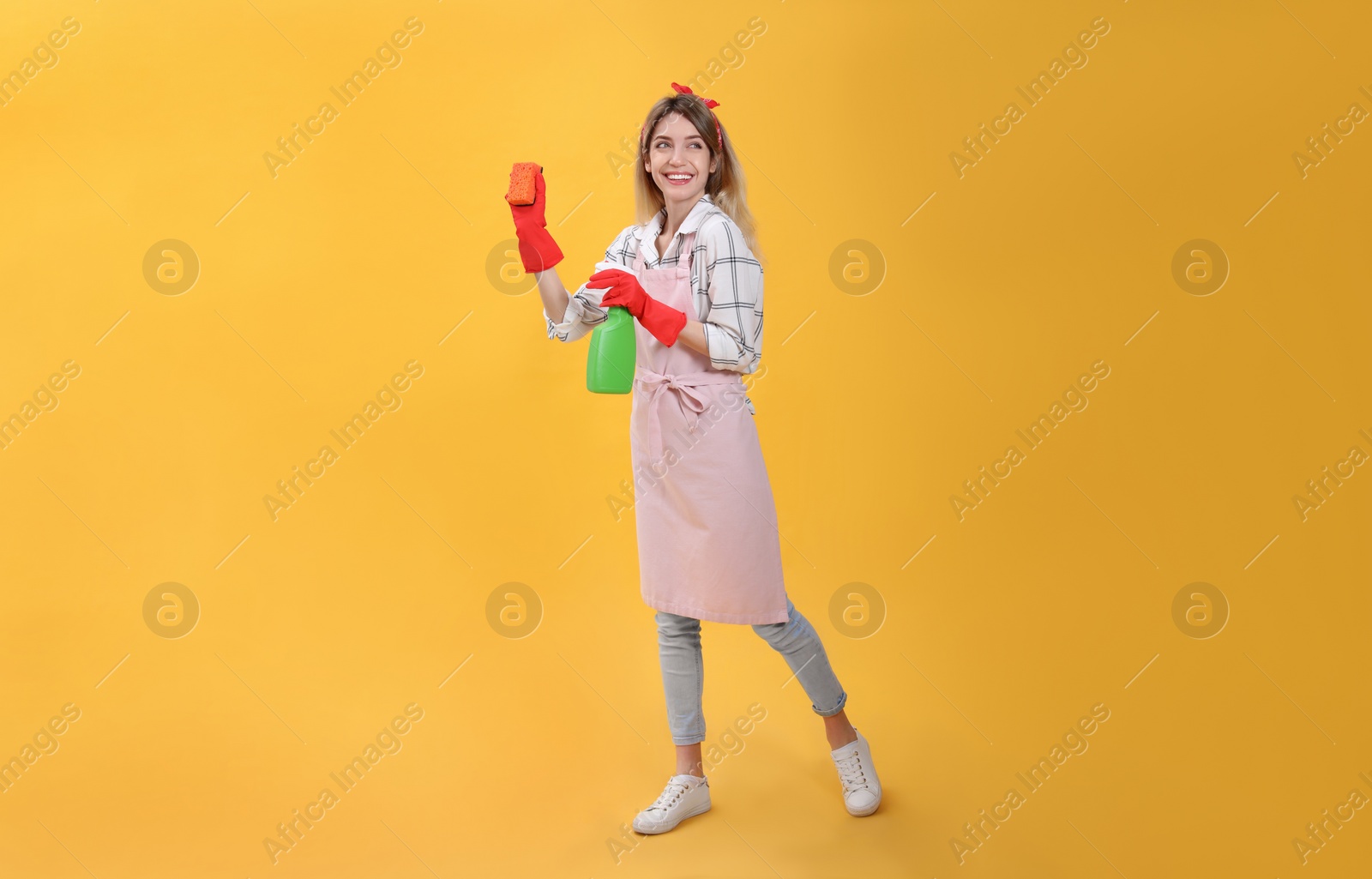 Photo of Young housewife with detergent and sponge on yellow background