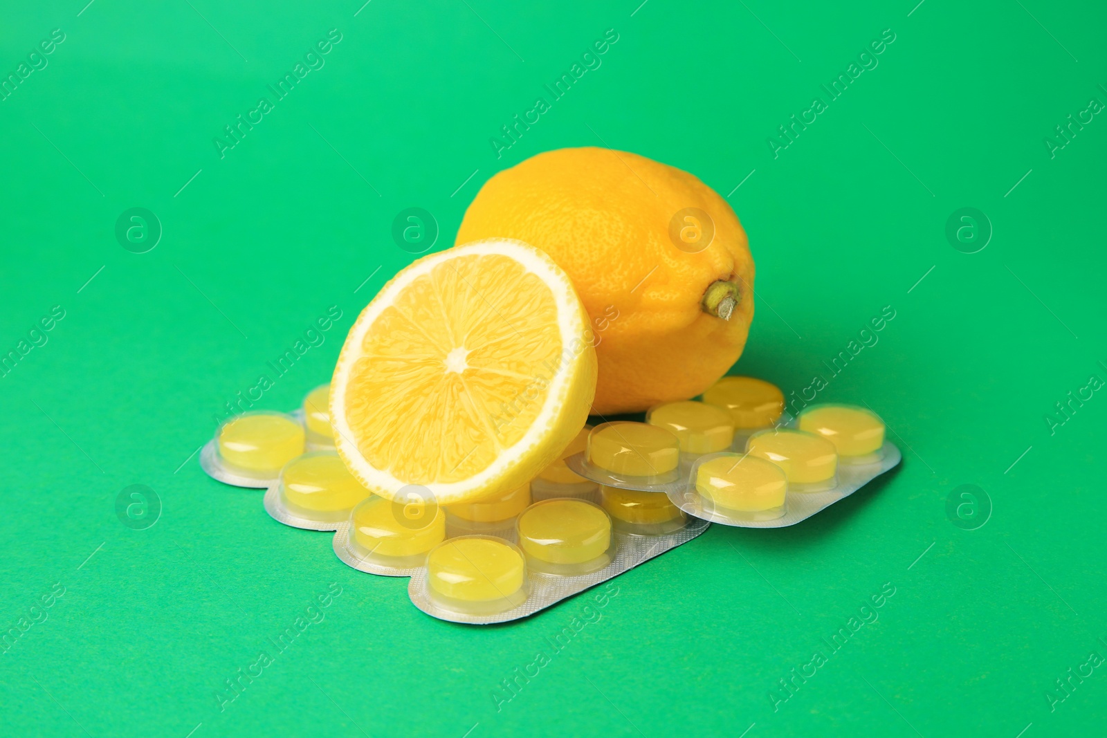 Photo of Blisters with cough drops and fresh lemons on green background