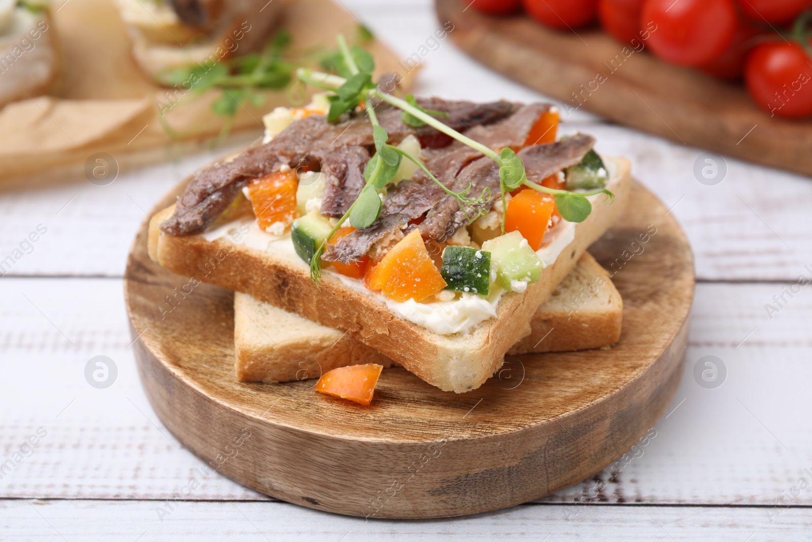 Photo of Delicious toasts with anchovies, cream cheese, bell peppers and cucumbers on white wooden table, closeup