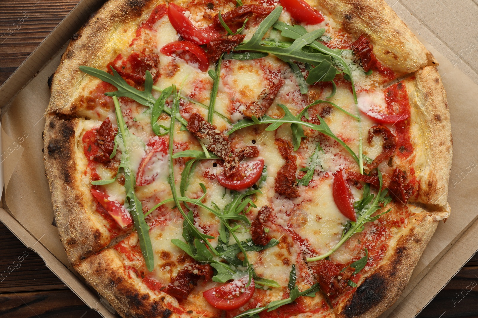 Photo of Tasty pizza with cheese, tomato and arugula in cardboard box on wooden table, top view