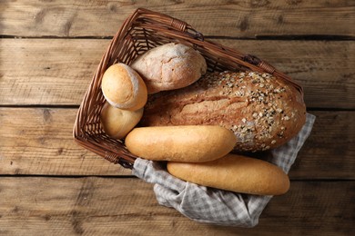 Photo of Wicker basket with different types of bread on wooden table, top view