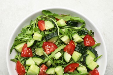 Photo of Delicious salad with cucumbers, tomatoes and sesame in bowl on light table, top view