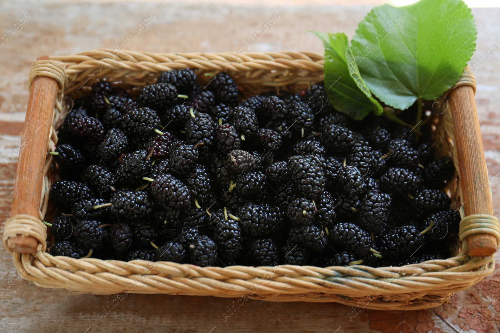 Photo of Wicker basket with delicious ripe black mulberries on wooden table