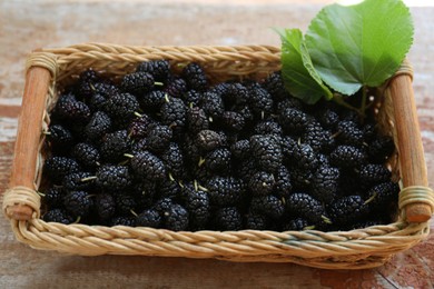 Photo of Wicker basket with delicious ripe black mulberries on wooden table