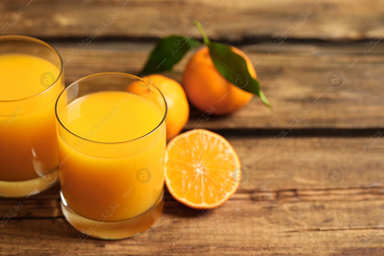 Photo of Glasses of fresh tangerine juice and fruits on wooden table. Space for text