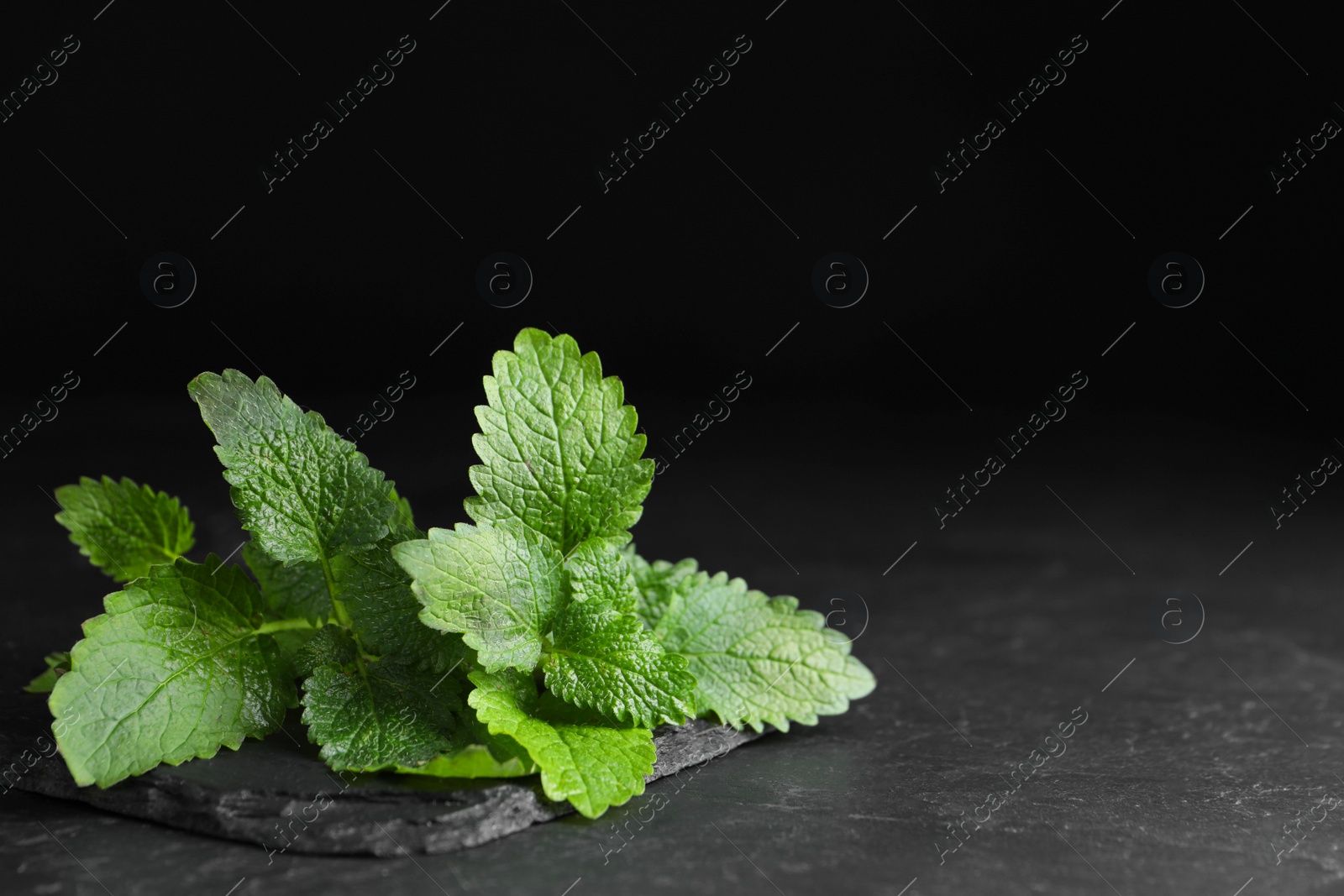 Photo of Fresh green lemon balm leaves on black table, space for text