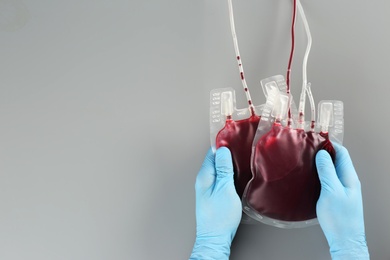 Photo of Doctor in gloves holding blood packs on gray background, top view with space for text. Donation day