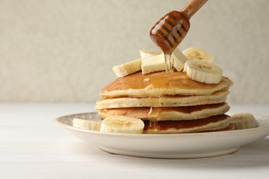 Photo of Pouring honey from dipper onto delicious pancakes with bananas and butter at white wooden table, closeup. Space for text