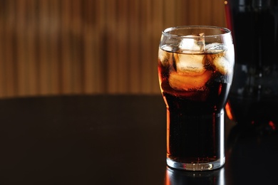 Glass of cola with ice and bottle on table against blurred background. Space for text