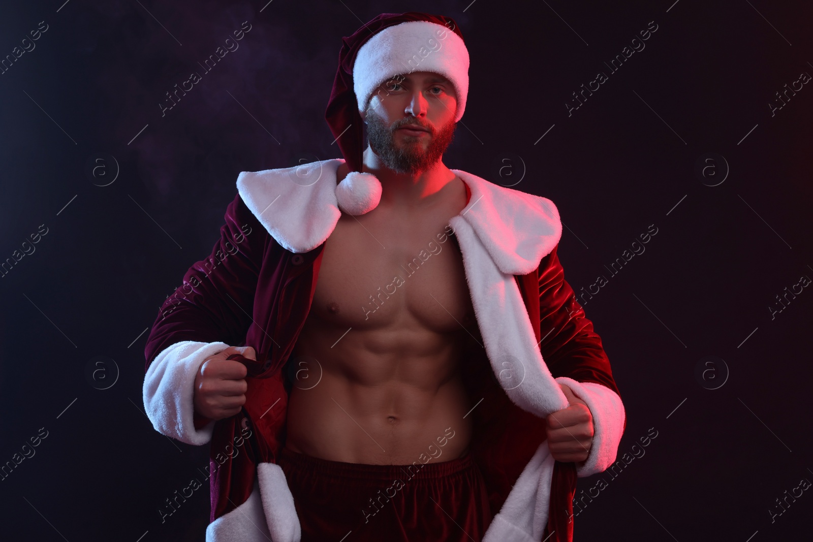 Photo of Attractive young man with muscular body in Santa costume on black background