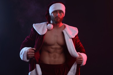 Photo of Attractive young man with muscular body in Santa costume on black background