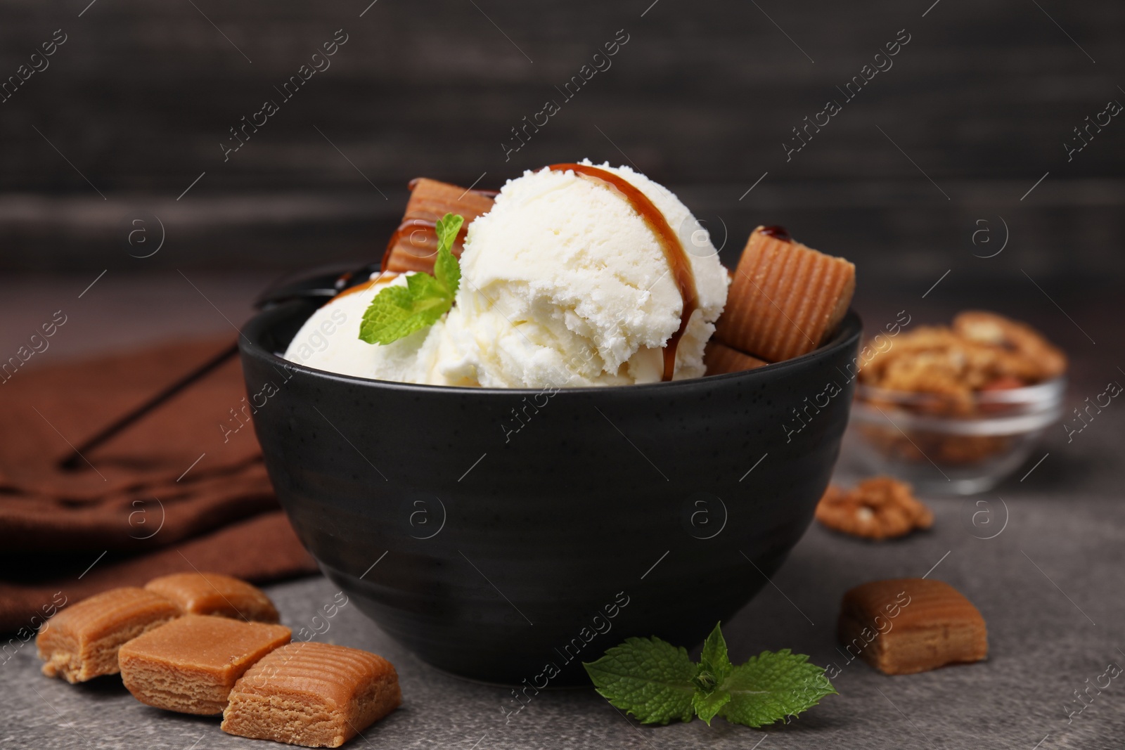 Photo of Bowl of tasty ice cream with caramel sauce, candies and mint on brown table, closeup