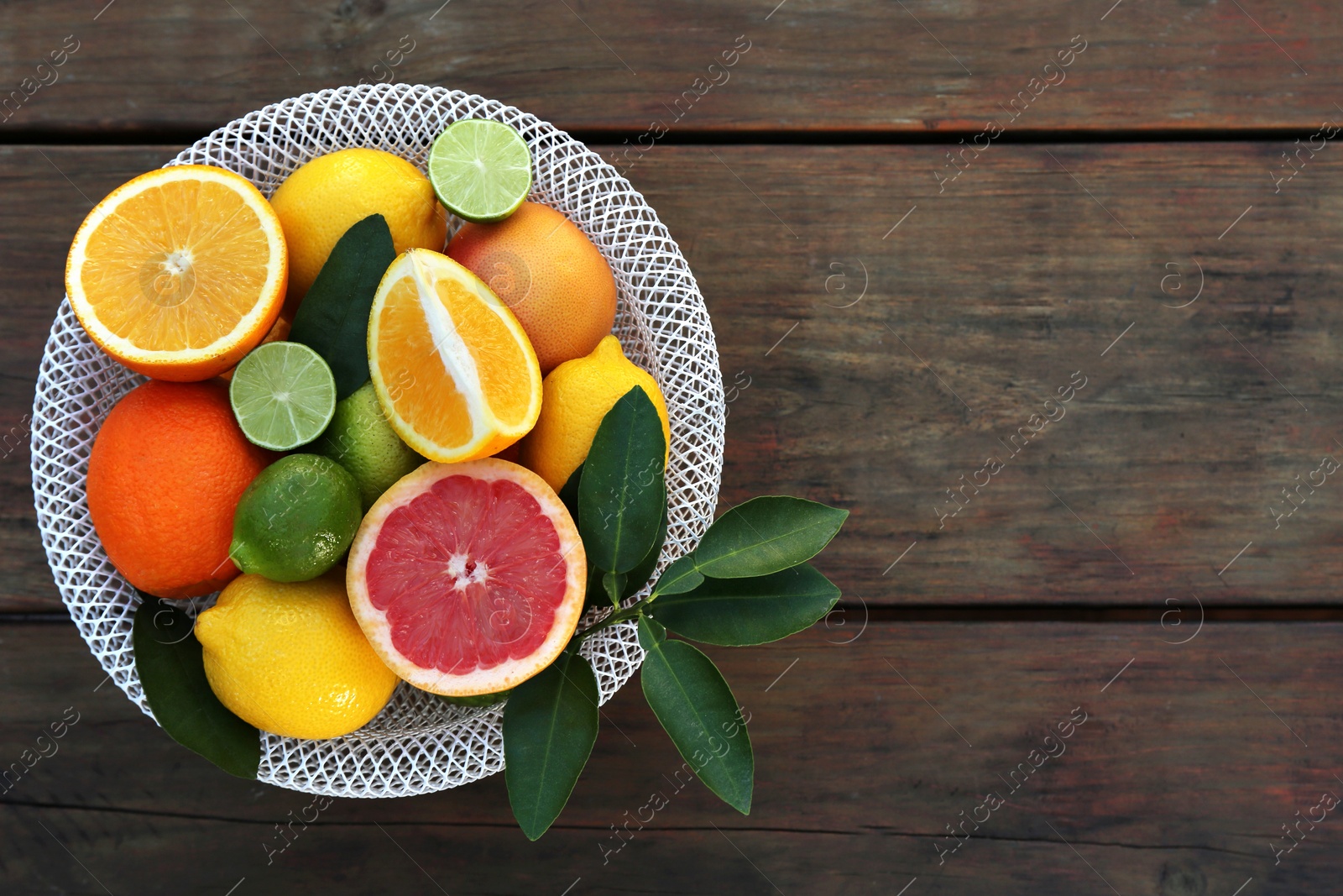 Photo of Bowl with different citrus fruits and leaves on wooden table, top view. Space for text