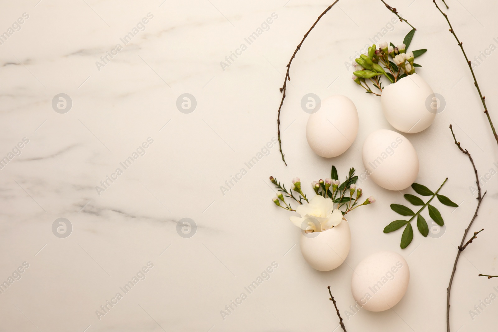 Photo of Easter eggs and beautiful flowers on white marble table, flat lay. Space for text