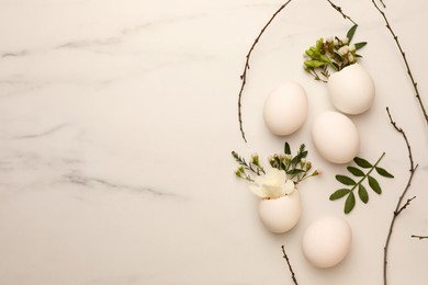 Easter eggs and beautiful flowers on white marble table, flat lay. Space for text