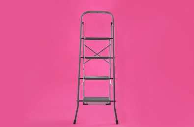 Photo of Modern metal stepladder on pink background. Construction tool