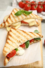 Photo of Delicious grilled sandwiches with mozzarella, tomatoes and basil on wooden board, closeup