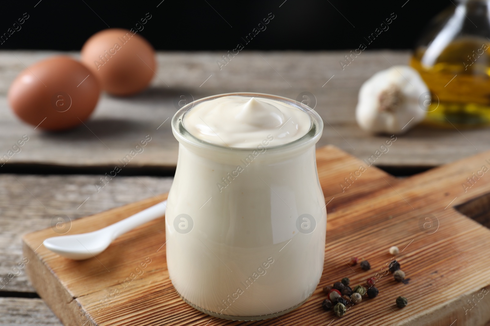 Photo of Fresh mayonnaise sauce in glass jar and ingredients on wooden table, closeup