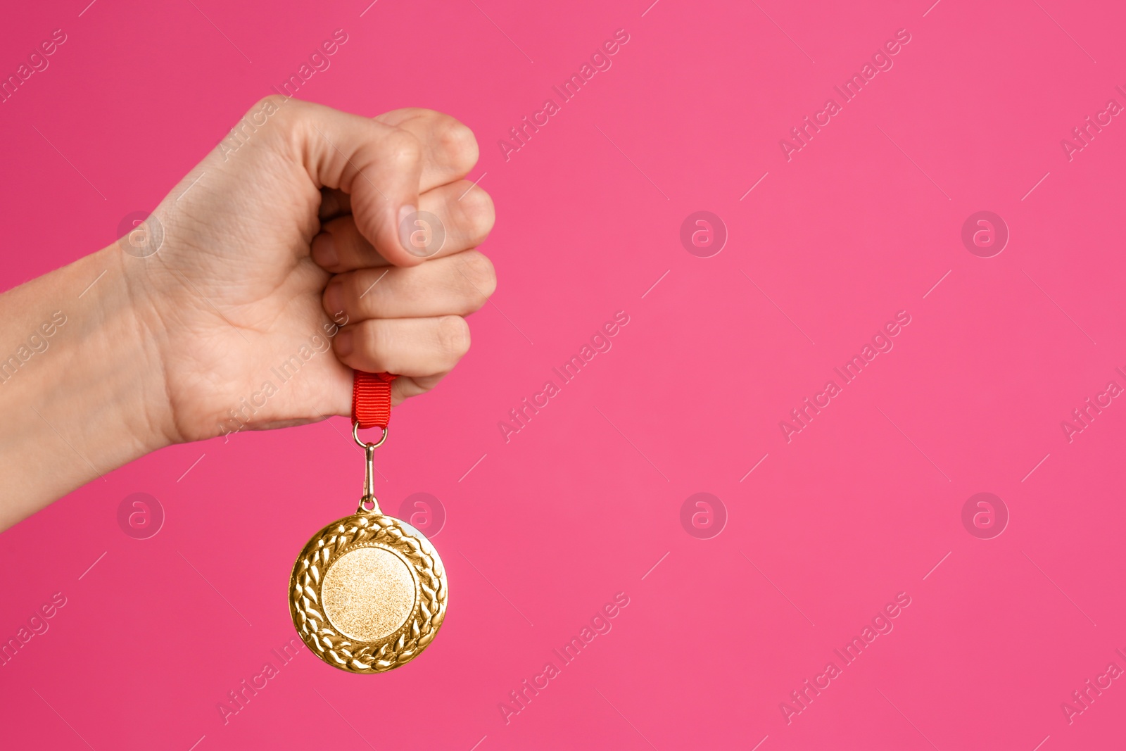 Photo of Woman holding golden medal on pink background, closeup. Space for design