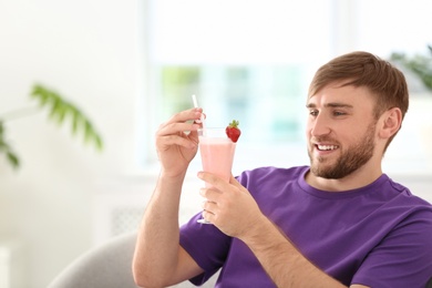 Young man with glass of delicious milk shake indoors