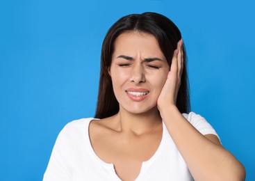 Young woman suffering from ear pain on light blue background