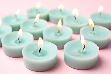 Burning light blue decorative candles on pink background