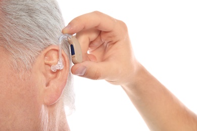 Photo of Young man putting hearing aid in father's ear on white background, closeup