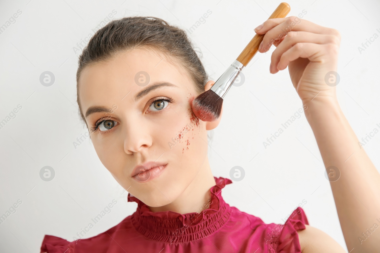 Photo of Young woman applying makeup on light background. Professional cosmetic products