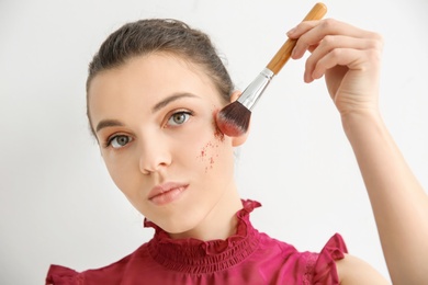 Young woman applying makeup on light background. Professional cosmetic products