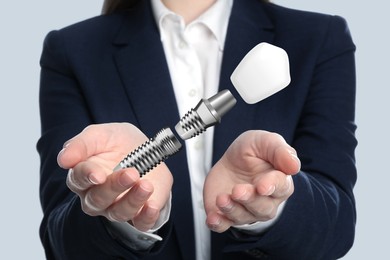 Woman demonstrating dental implant on light background, closeup