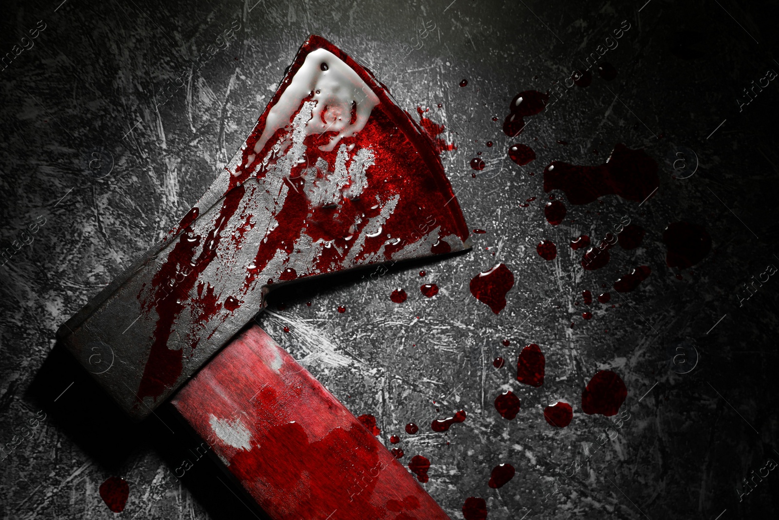 Photo of Axe with blood on dark gray textured surface in darkness, top view