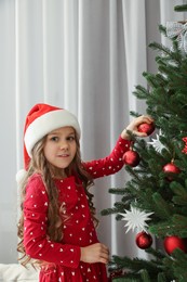Photo of Happy little girl decorating Christmas tree at home