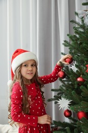 Happy little girl decorating Christmas tree at home