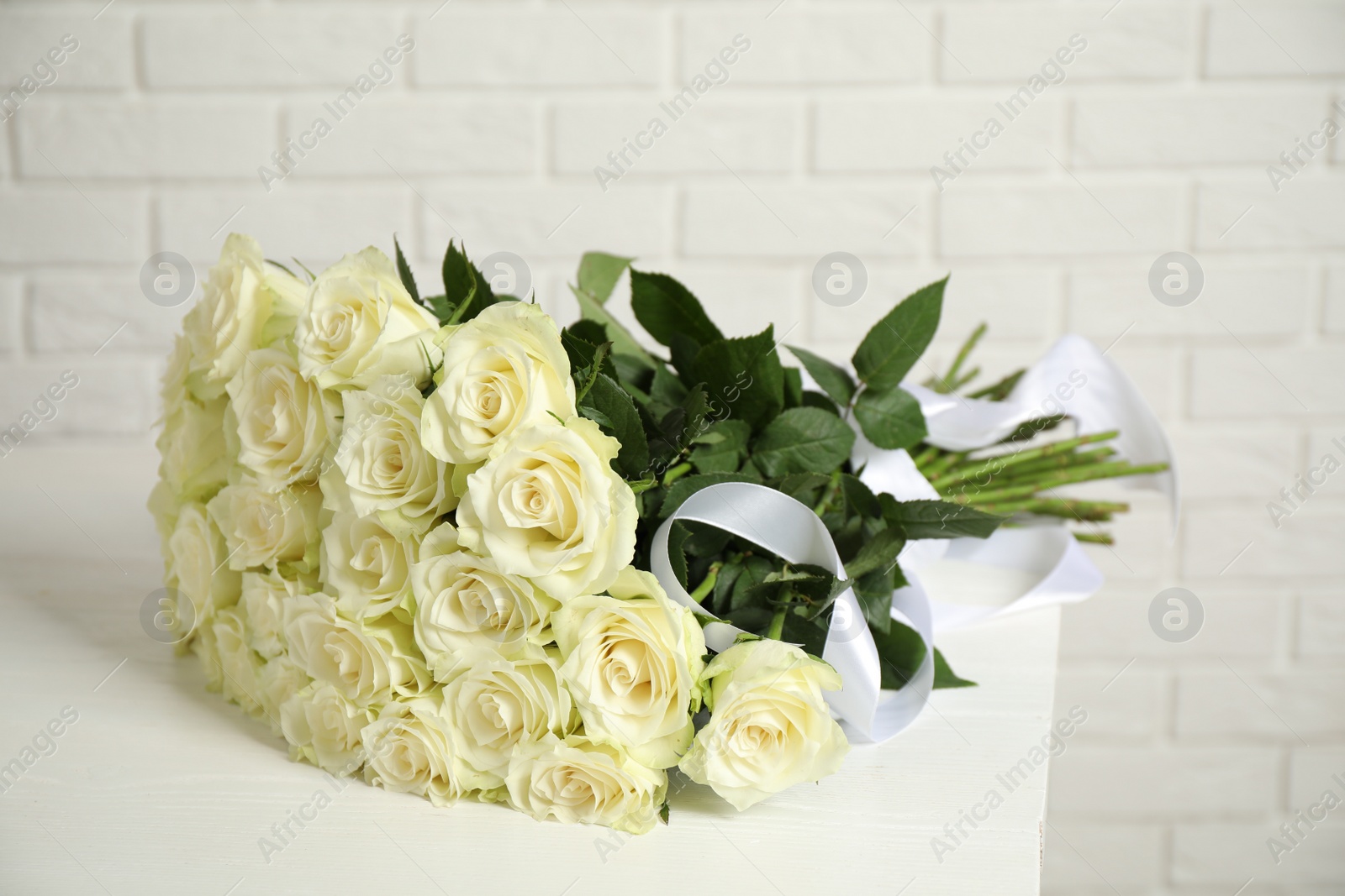 Photo of Luxury bouquet of fresh roses on table near white brick wall