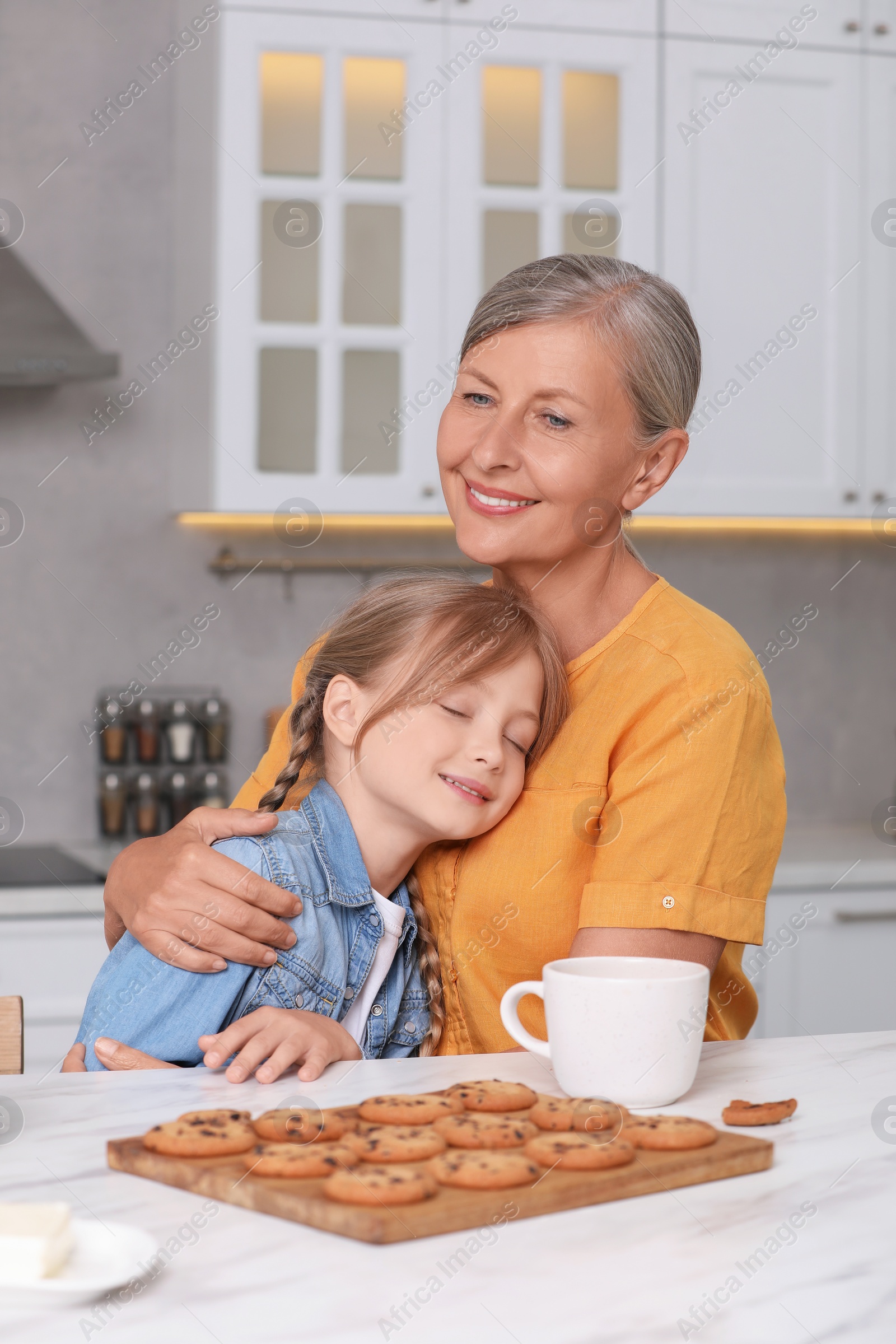 Photo of Happy grandmother hugging her granddaughter in kitchen