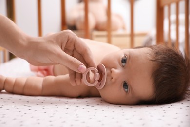 Photo of Mother giving pacifier to her cute little baby in crib at home, closeup
