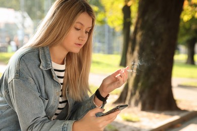 Young woman smoking cigarette while using smartphone outdoors