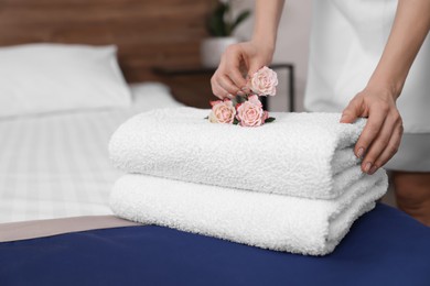 Photo of Chambermaid putting flowers on fresh towels in hotel room, closeup