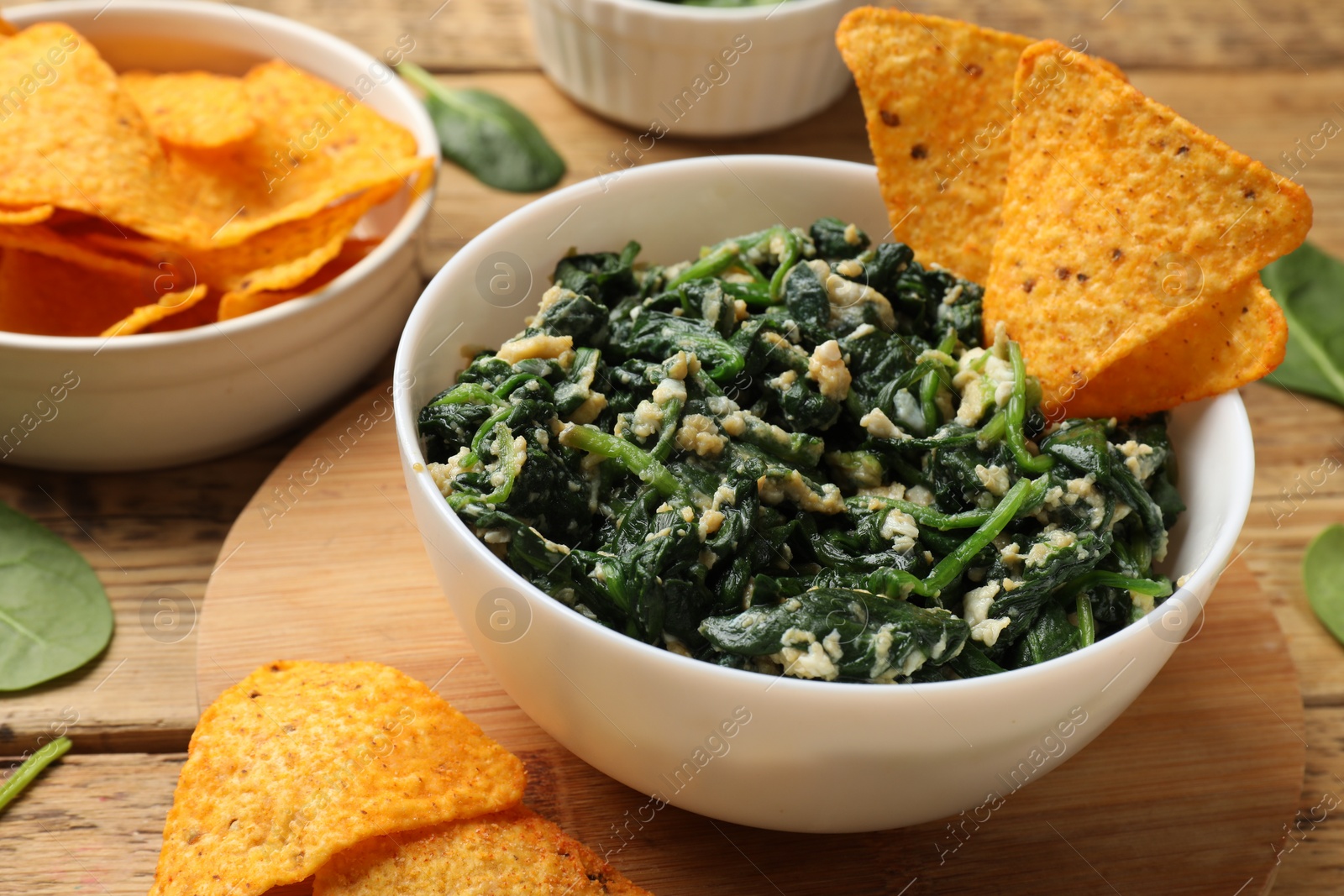 Photo of Tasty spinach dip with eggs in bowl and nachos chips on wooden table, closeup