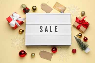 Lightbox with word Sale, gift boxes, credit card and Christmas decorations on beige background, flat lay